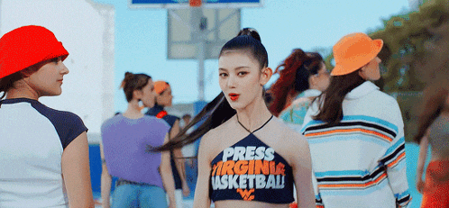a woman wearing a crop top that says press virginia basketball is standing in front of a crowd of people .