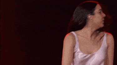 a woman in a white tank top is dancing and her hair is blowing in the wind