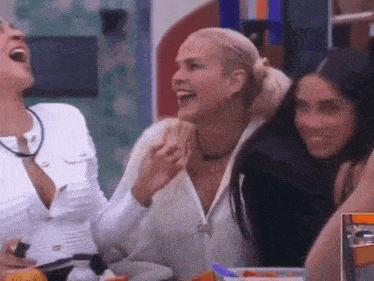 three women are sitting at a table laughing together .