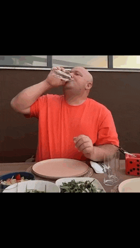 a man in a red shirt is drinking from a glass at a table