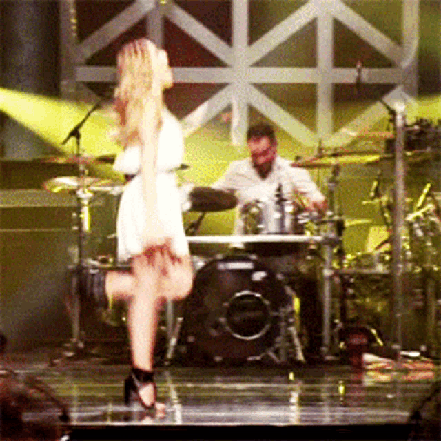 a woman in a white dress is dancing on a stage in front of a drum set
