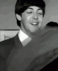 a black and white photo of a man in a suit and tie laughing with his eyes closed .