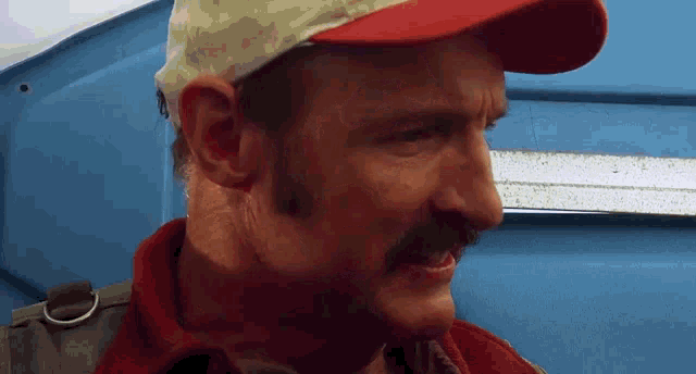 a man with a mustache wearing a hat and a red shirt