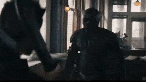 a man in a superhero costume is holding a gun and talking to another man in a room .