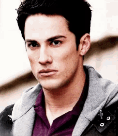 a man wearing a purple shirt and a gray jacket looks at the camera