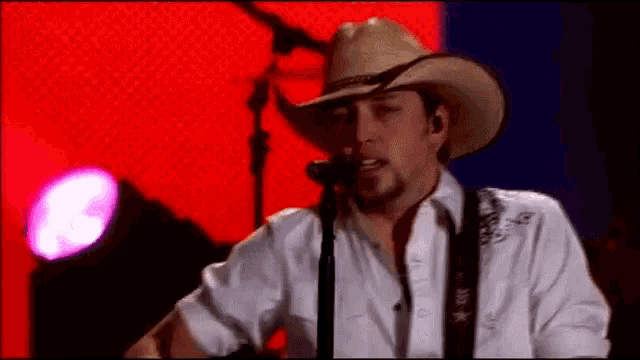 a man wearing a cowboy hat singing into a microphone