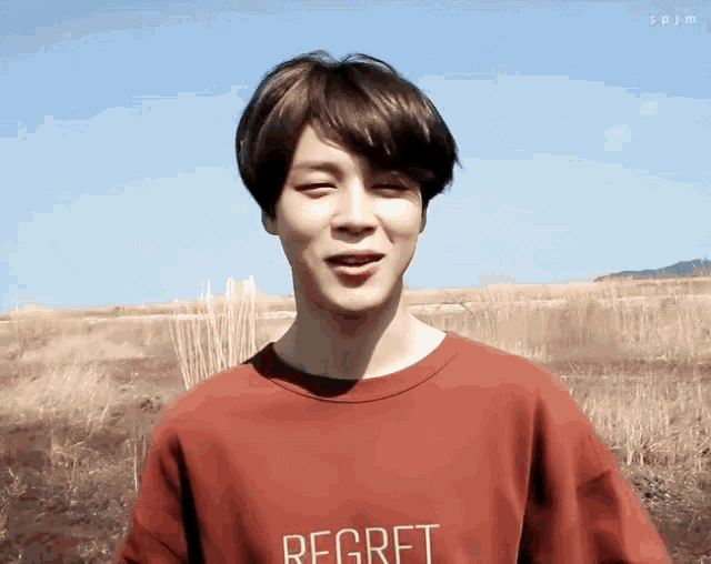 a young man wearing a red shirt that says regret is standing in a field