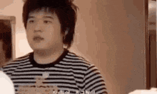 a man in a striped shirt is standing in front of a mirror and looking at himself .