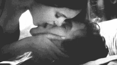 a black and white photo of a woman kissing a man on the neck .