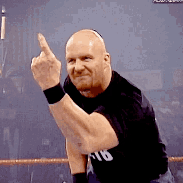 a bald wrestler is giving the middle finger in a wrestling ring .