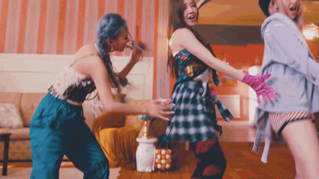 three women are dancing in a living room with a couch in the background