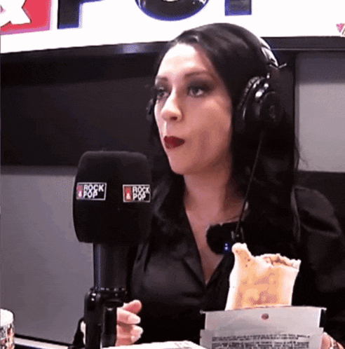 a woman wearing headphones is eating a taco in front of a microphone that says rock & pop