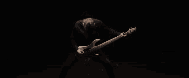 a man in a black shirt is playing a bass guitar in the dark