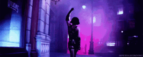 a woman is dancing on a street in front of a building in a dark room .