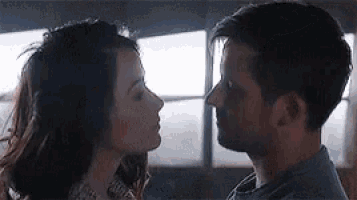 a man and a woman are looking at each other and kissing in front of a window .