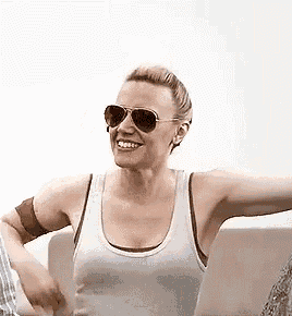 a woman wearing sunglasses and a tank top is sitting on a couch and smiling .