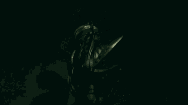 a person in a black suit is standing in the dark with a sword in their hand .