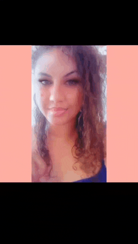 a woman with curly hair looks at the camera with a pink background