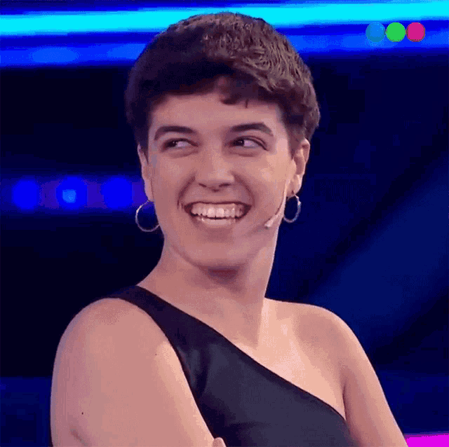 a woman wearing hoop earrings is smiling in front of a blue background