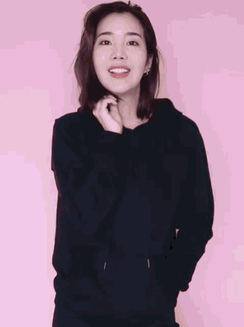 a woman wearing a black hoodie is smiling and holding her hands in her pockets