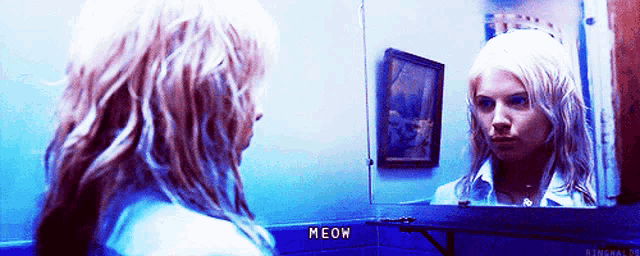 a woman looking at her reflection in a mirror with the word meow written on the wall