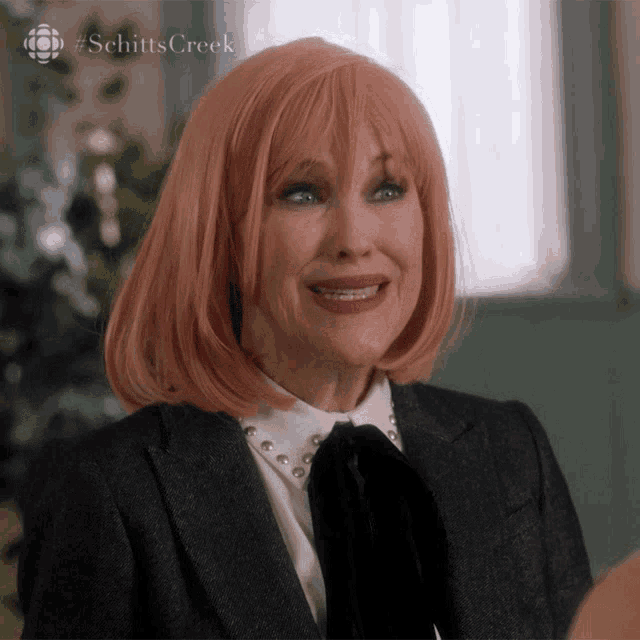 a woman wearing a pink wig and a suit is smiling with the hashtag schittscreek