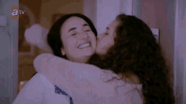 two women hugging each other with a tv logo behind them