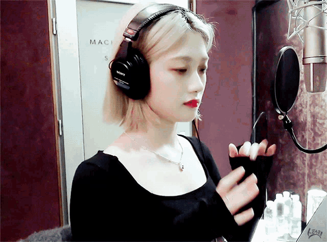 a woman wearing headphones stands in front of a microphone in a room that says mac