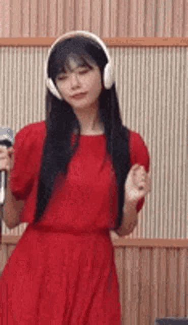 a woman in a red dress is wearing headphones and singing into a microphone .