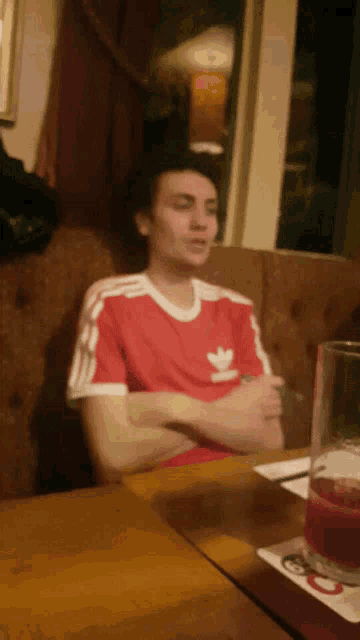 a man in an adidas shirt sits at a table with his arms crossed