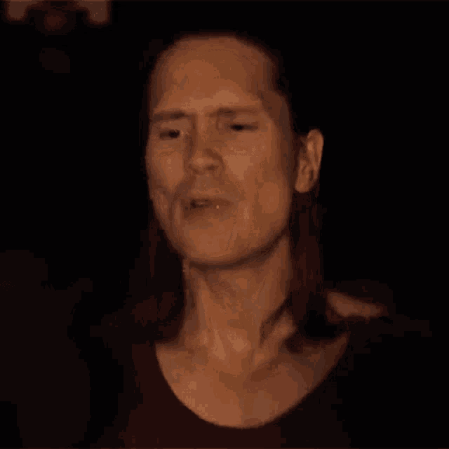 a man with long hair is smiling in the dark .