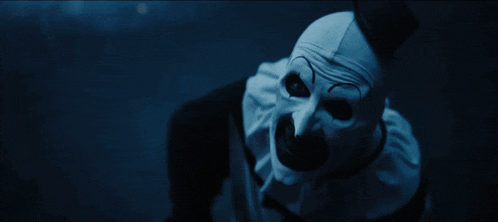 a clown is holding a trumpet in his hand in a dark room