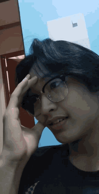 a young man wearing glasses holds his hand to his head