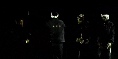 a group of men are standing in a dark room and one of them is wearing a bandana on his head .