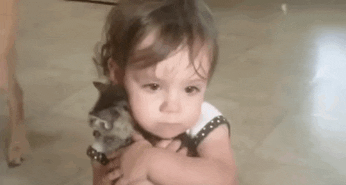 a little girl is holding a small kitten in her arms and making a face .