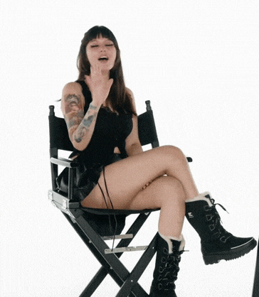 a woman is sitting on a director 's chair with her legs crossed and waving .