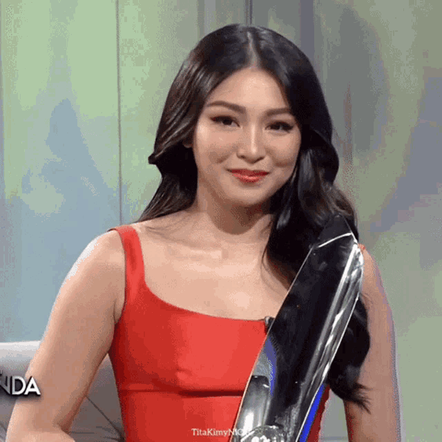 a woman in a red dress is holding a trophy and the word titakmyng is on the bottom right