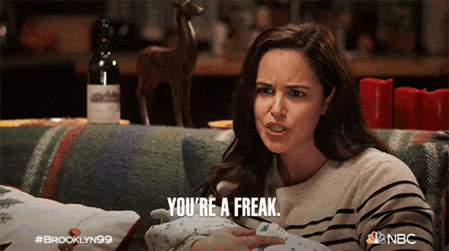 a woman is holding a baby and says " you 're a freak " while sitting on a couch