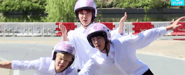 three people wearing pink motorcycle helmets are standing on a road in front of a vlive banner