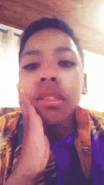 a young boy wearing a yellow shirt and purple tie is touching his face .