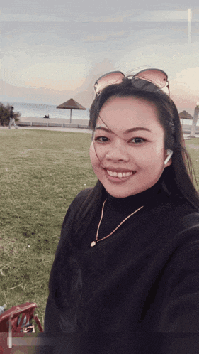 a woman wearing sunglasses and a necklace smiles for a selfie