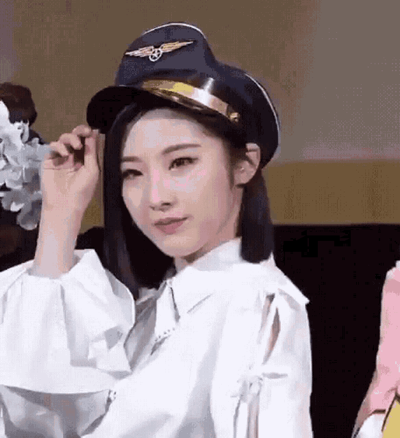 a woman wearing a pilot hat and a white shirt is looking at the camera .