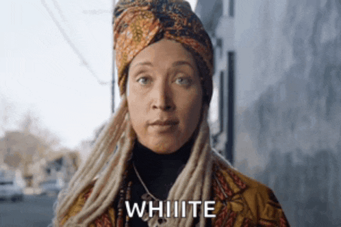 a woman with dreadlocks and a turban is standing in front of a building and says `` white '' .