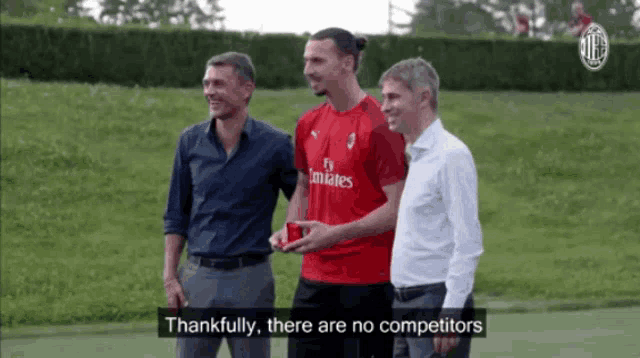 a man in a red fly emirates shirt stands between two men