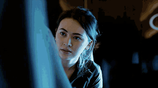 a woman is sitting in a dark room and looking out the window