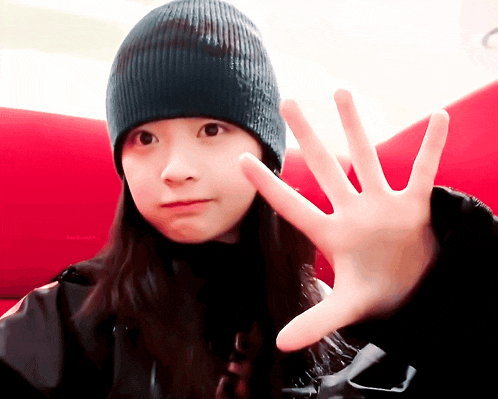a girl wearing a black beanie and a black jacket is making a stop sign with her hand