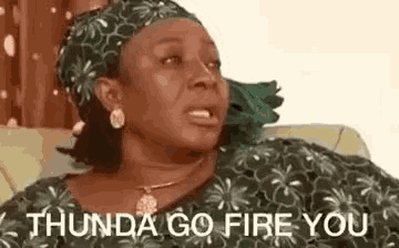a woman is sitting on a couch making a funny face and saying `` thunda go fire you '' .