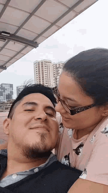 a woman kissing a man 's forehead with a building in the background