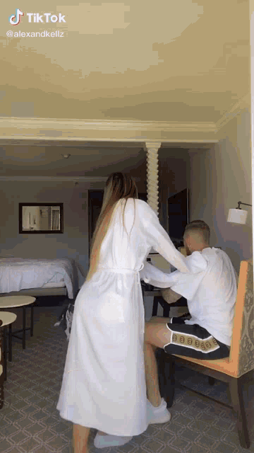 a woman in a robe is standing next to a man sitting in a chair .