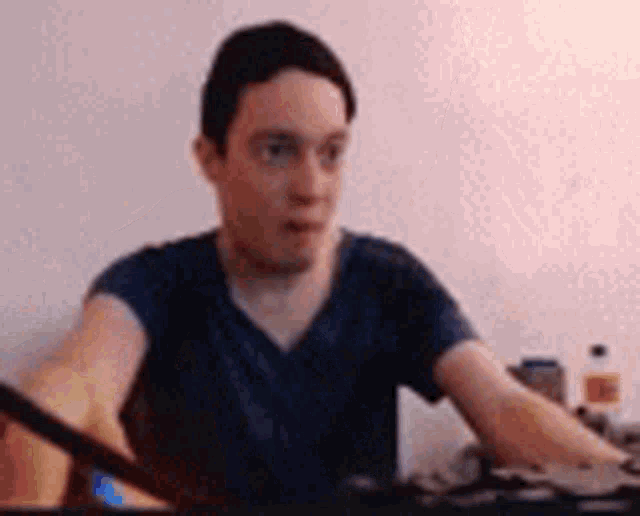 a man in a blue shirt is sitting at a table with his hands on his knees .